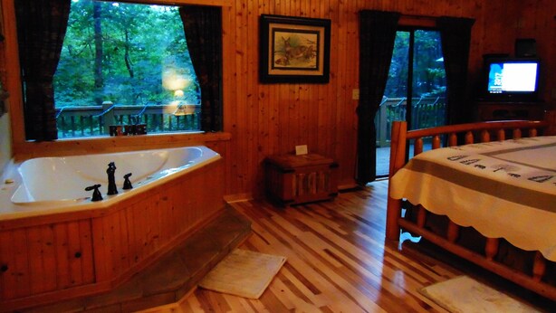 Un bagno in una baita di legno con una grande vasca, una panca in legno e un televisore.