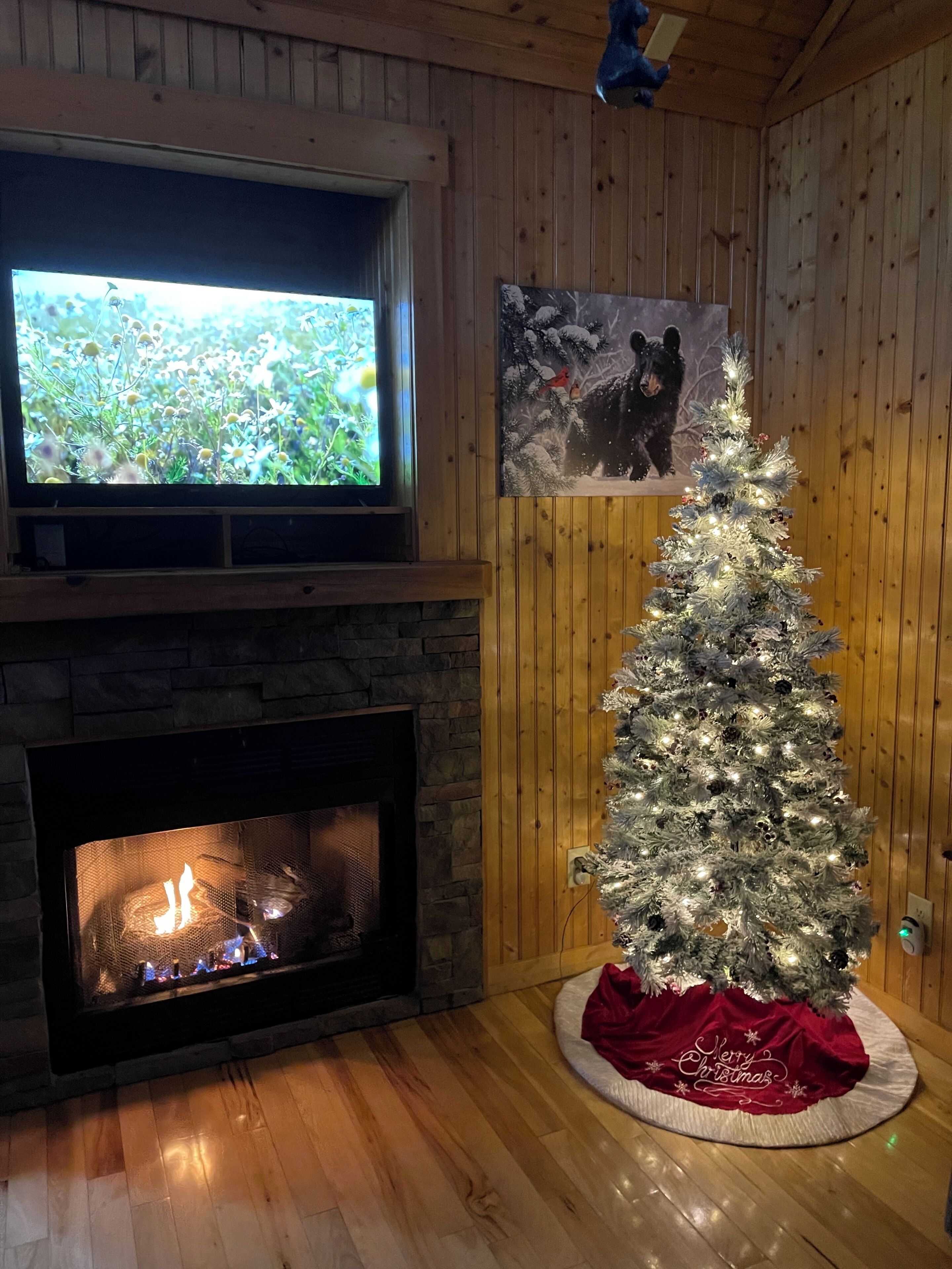 Une pièce chaleureuse avec une cheminée en pierre, un téléviseur fixé au-dessus et un sapin de Noël illuminé.