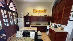 A compact kitchen with wooden cabinets, a dining table with floral cushions, a microwave, and a stove. - Gorgeous Views of Pacific and Rainforest (Manuel Antomio)