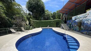 A swimming pool with a tiled edge, surrounded by a concrete deck and a green fence. - Gorgeous Views of Pacific and Rainforest (Manuel Antomio)