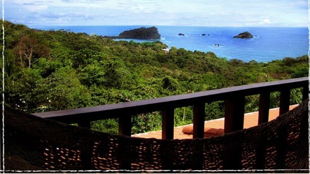 A view from a balcony overlooking a lush green landscape with a clear blue sea and small islands in the distance. - Gorgeous Views of Pacific and Rainforest (Manuel Antomio)