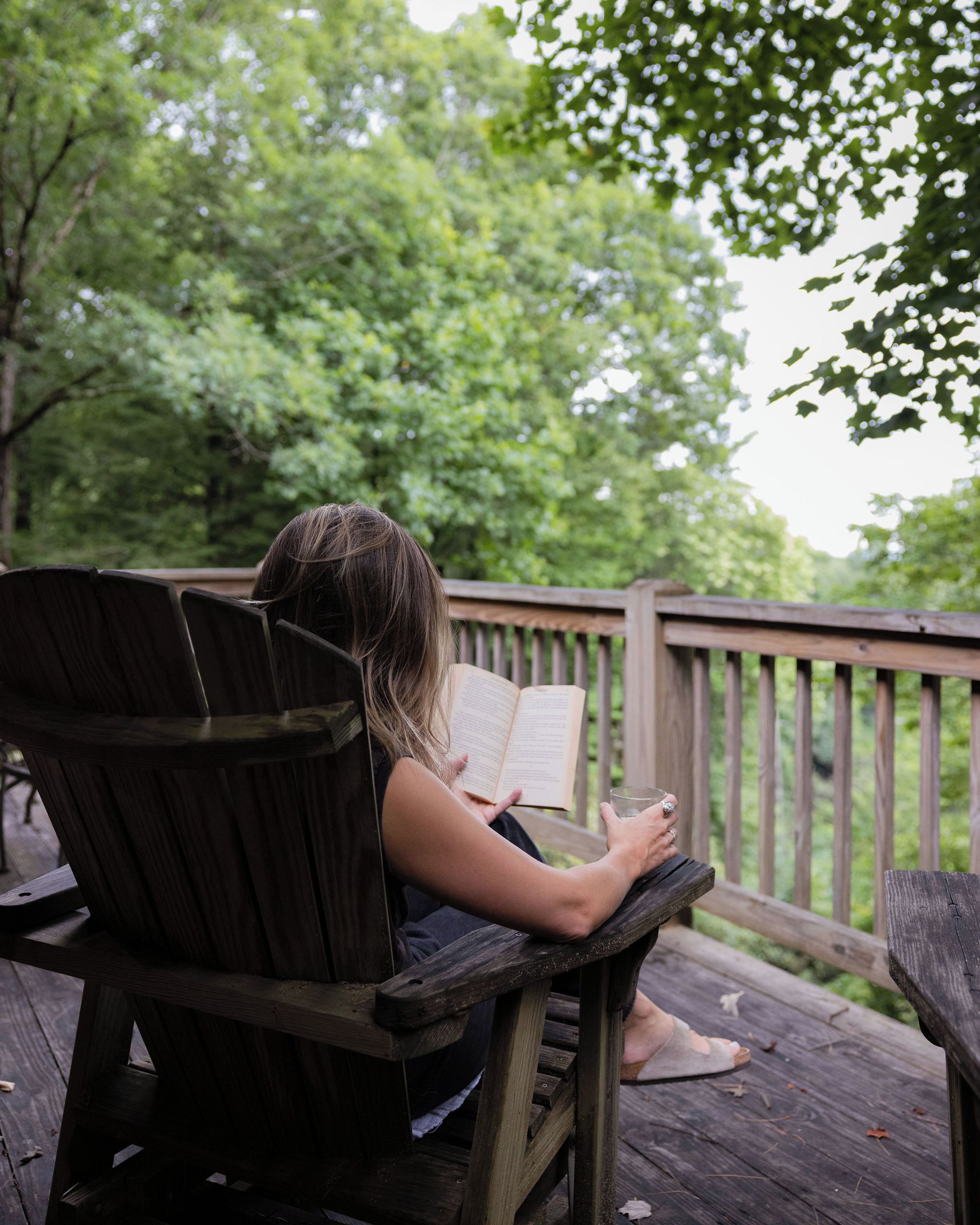 Eine Person sitzt auf einem Holzdeckstuhl und liest ein Buch.
