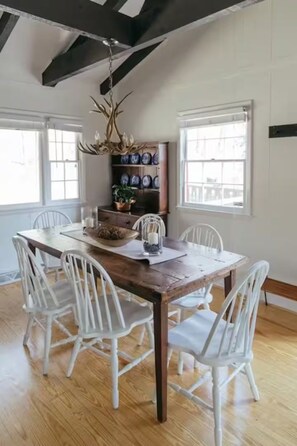 A dining area with a wooden table, white chairs, a chandelier, and a wall-mounted shelf with decorative plates.