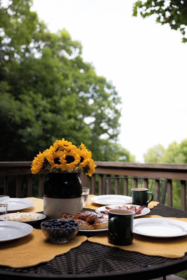 Une table à manger avec des assiettes, un bol de myrtilles, une tasse et un vase rempli de fleurs jaunes.