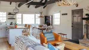 A spacious living room with a sofa, chairs, and a coffee table. There is a kitchen area with a dining table and chairs. A chandelier hangs from the ceiling, and a door is visible in the background. - The Dala House | Scandinavian Retreat in Blowing Rock (Blowing Rock)