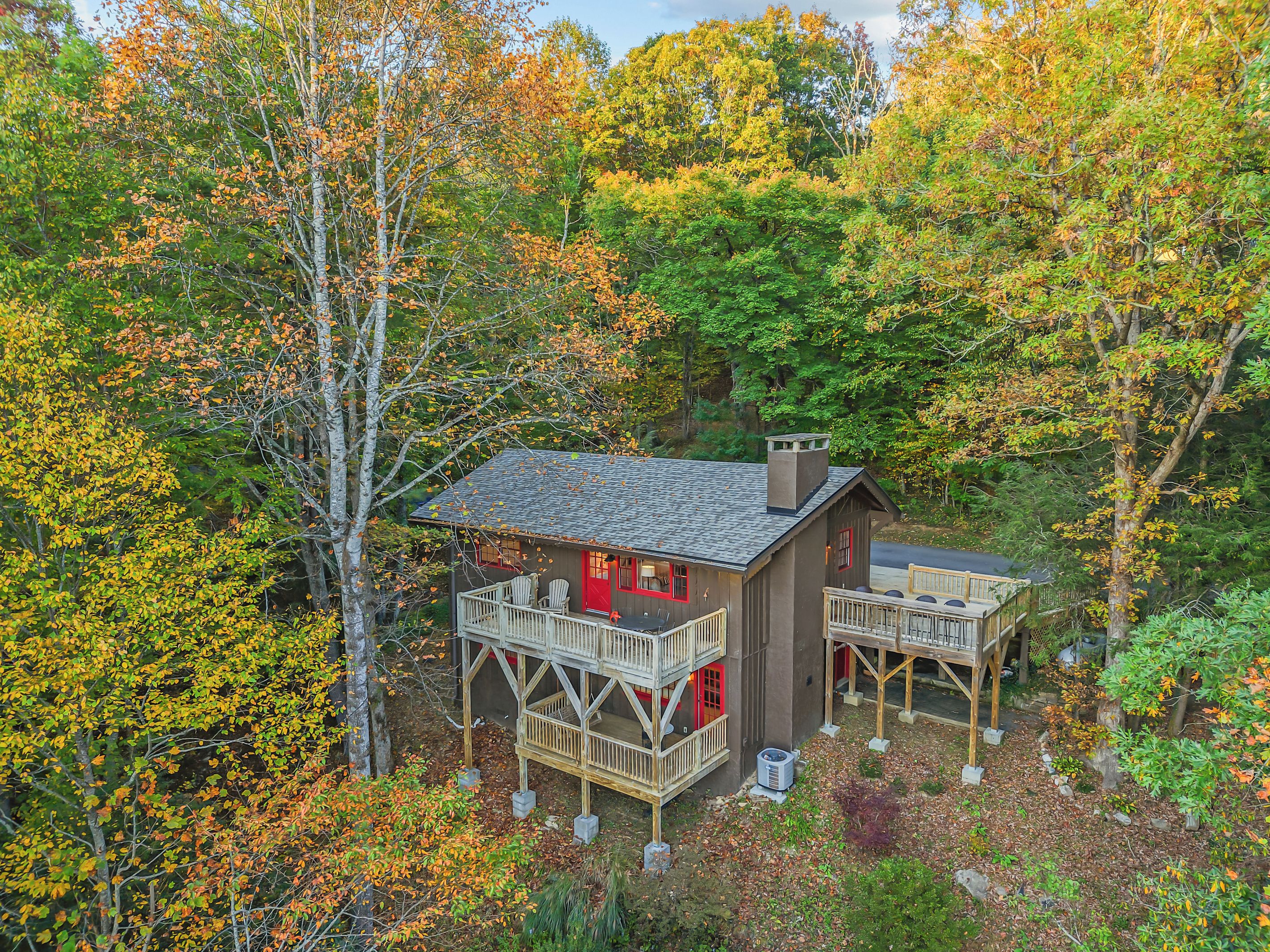 Une cabane dotée d’une terrasse, entourée d’arbres aux feuilles d’automne.