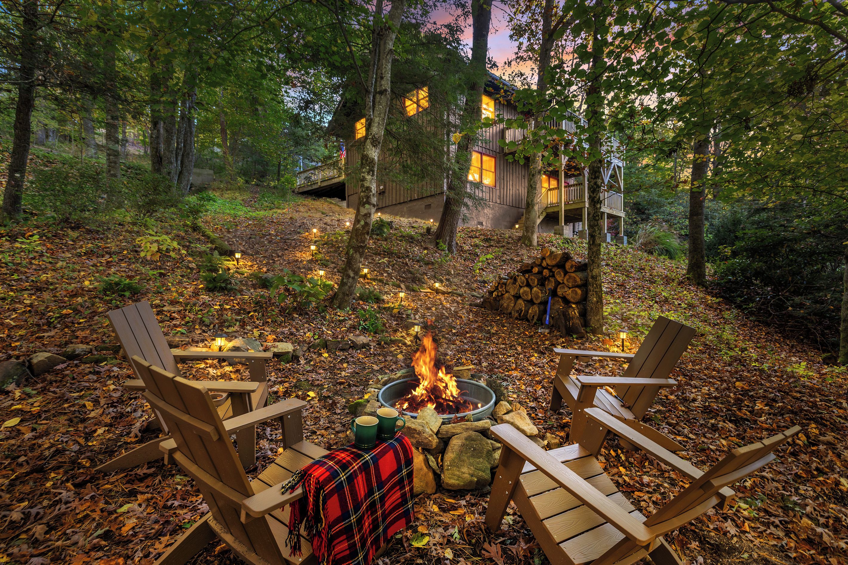 A cabin with a fire pit and two chairs in a forest setting.