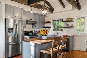 A modern kitchen with stainless steel appliances, a wooden island, and a view of greenery outside.