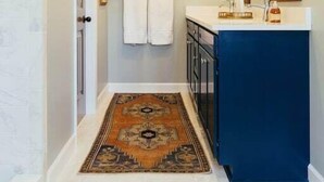 A bathroom with a white tiled floor, a blue vanity, a mirror, and a patterned rug. - The Dala House | Scandinavian Retreat in Blowing Rock (Blowing Rock)