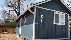 A small, single-story house with a dark blue exterior, numbered 316, and a security sign indicating it is protected by AccessOne. - Newly Remodeled  Pet Friendly Cottage (Colorado Springs)