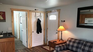 A cozy living room with a plaid sofa, a small wooden table with a lamp, and a kitchen area with a microwave. - Newly Remodeled  Pet Friendly Cottage (Colorado Springs)