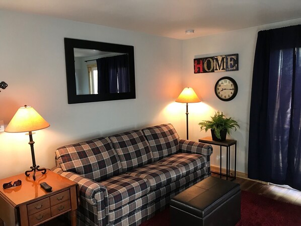 A living room with a plaid sofa, two lamps, a clock, a mirror, and a plant.
