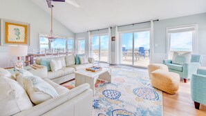 A spacious living room with a large window, a ceiling fan, and a view of the beach. - Oceanfront Dog Friendly Home in Waves w/ Private Pool, Hot Tub, Tiki Bar, Grill (Waves)