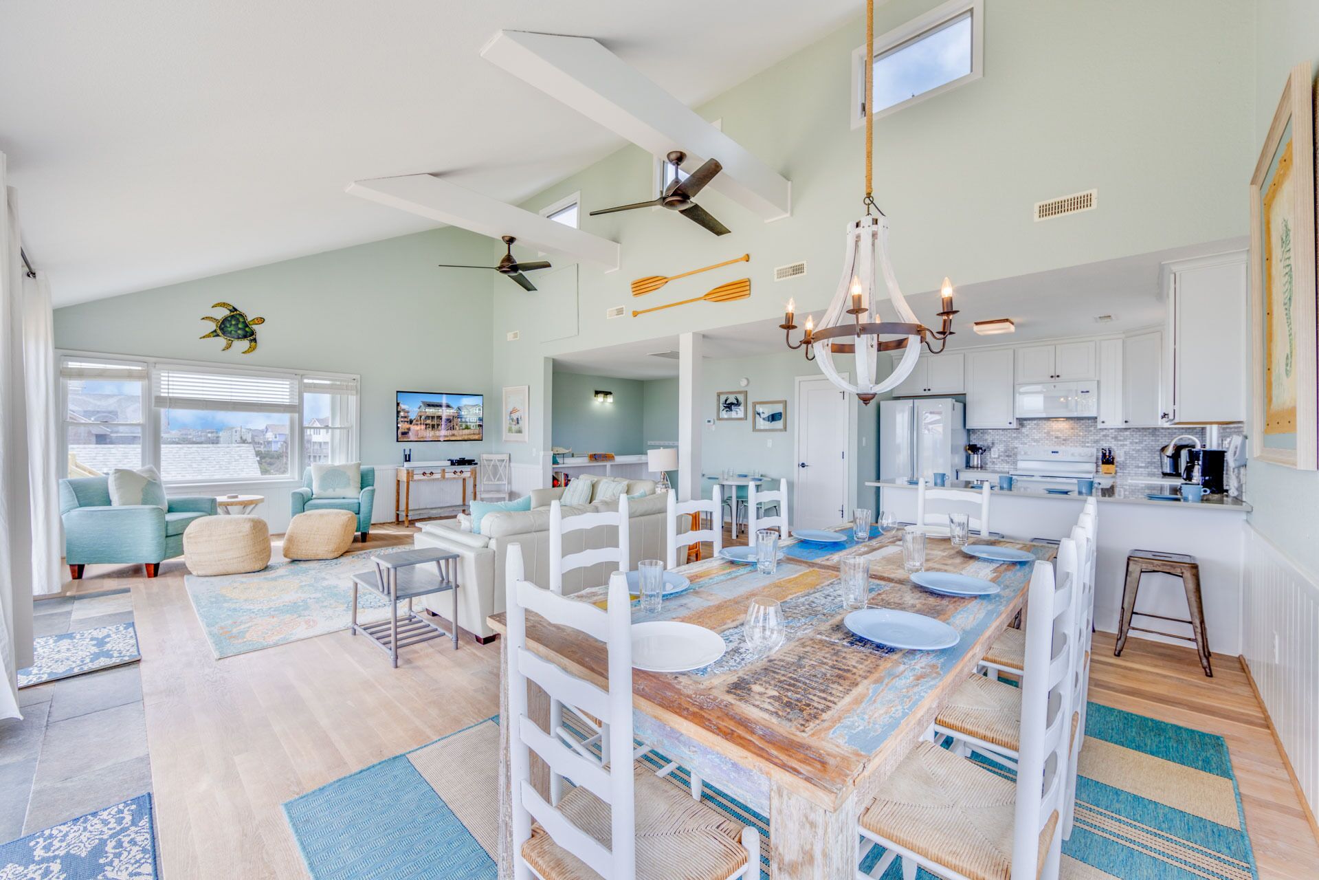 A spacious living area with a large wooden dining table, white furniture, and a ceiling fan.