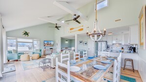 A spacious living area with a large wooden dining table, white furniture, and a ceiling fan. - Oceanfront Dog Friendly Home in Waves w/ Private Pool, Hot Tub, Tiki Bar, Grill (Waves)