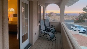Un balcon donnant sur un coucher de soleil, un panneau de signalisation indiquant un arrêt obligatoire et une voiture garée.
