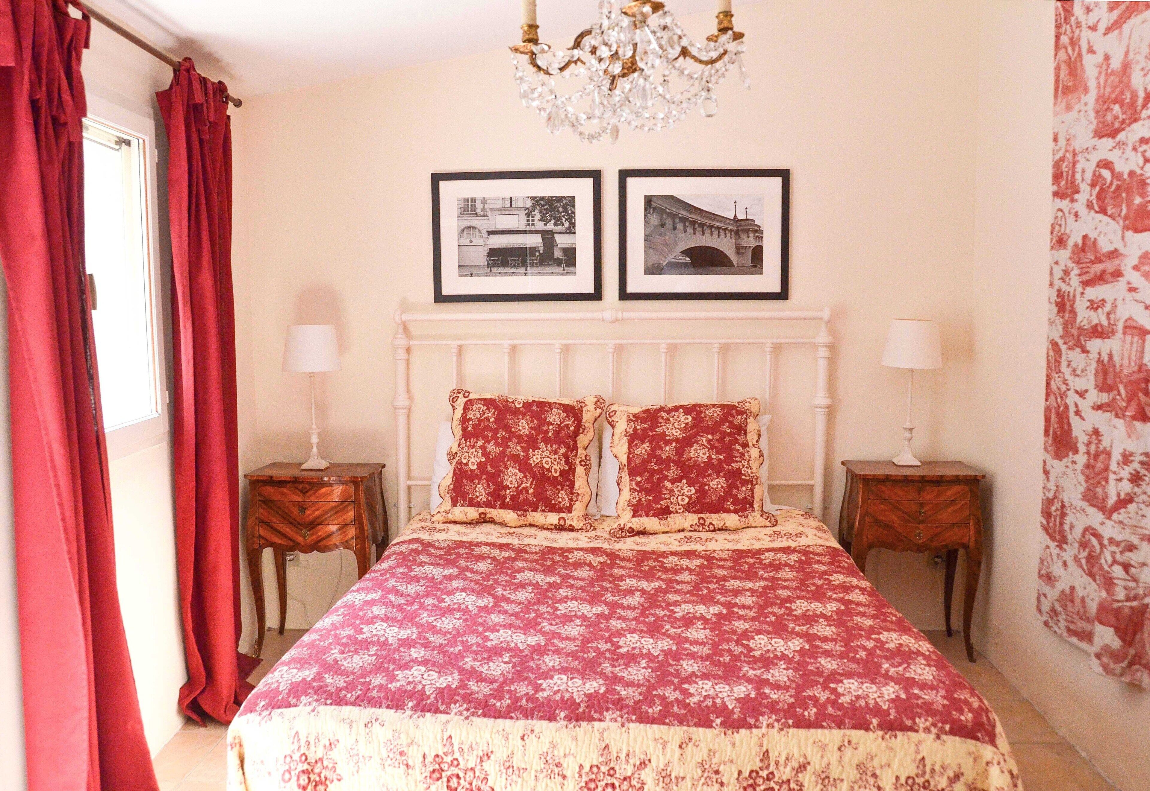 Une chambre à coucher avec un lit, deux tables de chevet, un lustre et deux tableaux encadrés accrochés au mur.