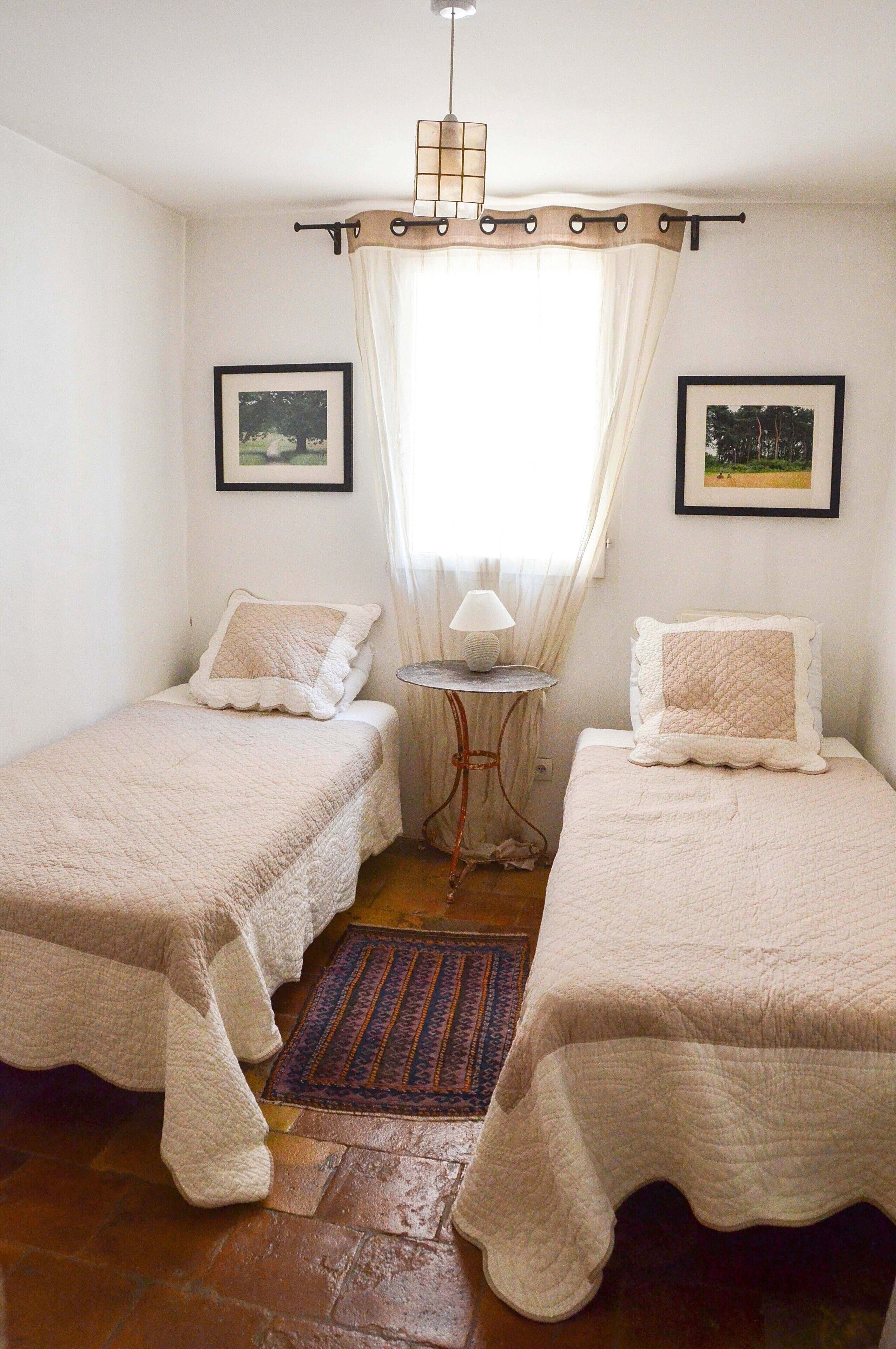 Une petite chambre à coucher, chaleureuse et accueillante, avec deux lits, une petite table avec une lampe et une fenêtre avec des rideaux.