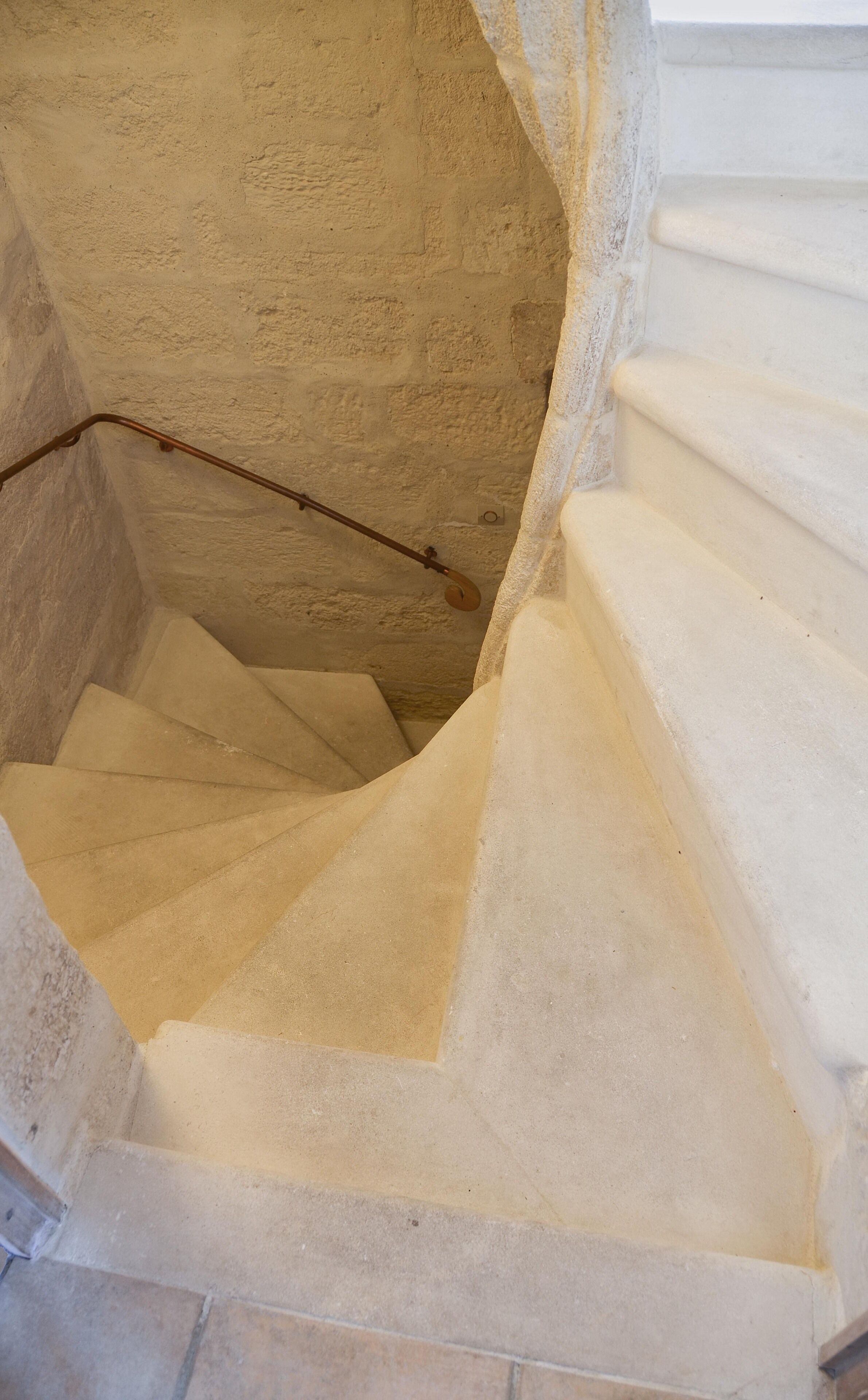 A spiral staircase with a textured wall and a metal handrail.