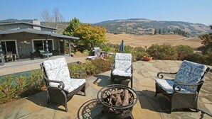 A patio with wicker chairs and a fire pit, overlooking a scenic landscape. - Wine Country Retreat with Pool, Vineyard, Trampoline, Putting Green and Hot Tub (Santa Rosa)