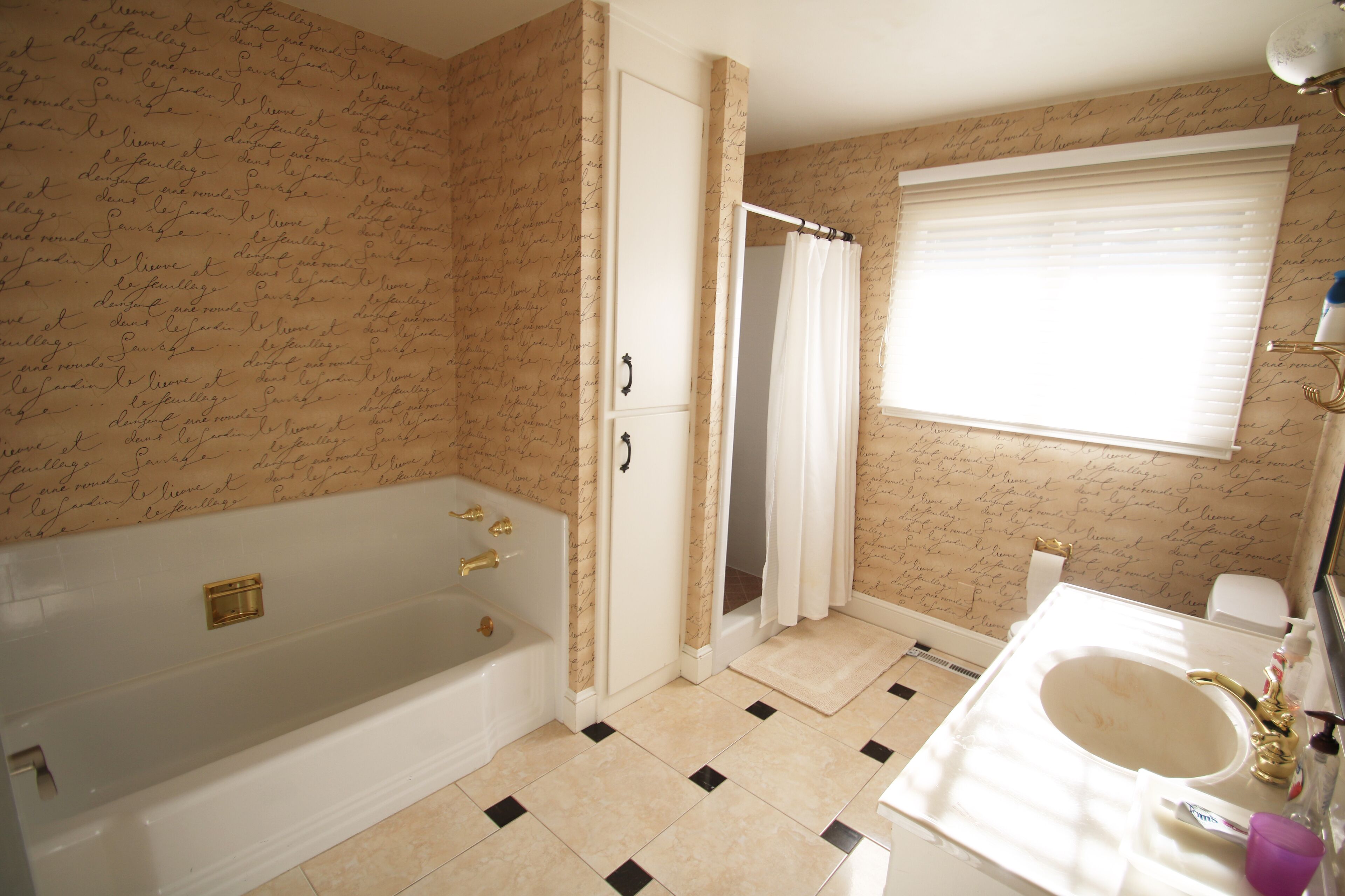 A bathroom with a bathtub, toilet, sink, and a window with a curtain.