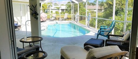Ein überdachter Außenbereich mit Pool, Korbmöbeln und Blick auf die umliegende Bepflanzung.