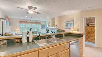 A kitchen with a double sink, wooden cabinets, a ceiling fan, and a window with a view of greenery.