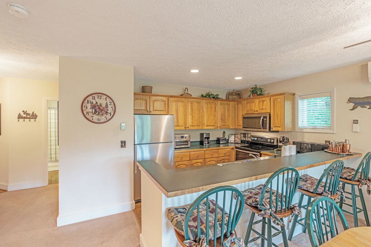 A kitchen with wooden cabinets, a stainless steel refrigerator, a microwave, and a large island with bar stools.