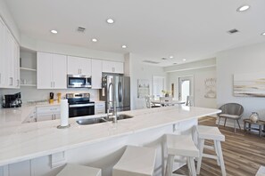 A modern kitchen with white cabinetry, stainless steel appliances, and a central island with bar stools. - Beautiful Beach House  - Private Pool -Great Views -Gulf of America (Gulf Shores)