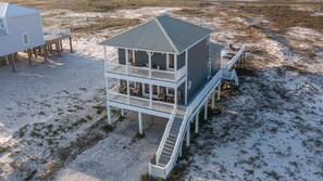 A two-story beach house with a balcony and a deck, surrounded by sand and sparse vegetation. - Beautiful Beach House - Private Pool -Great Views -Gulf of America (Gulf Shores)
