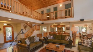 A spacious living area with a wooden staircase, leather sofas, a coffee table, and a dining area in the background. - Kantor's Hideout: Ample TD Home with Private Hot Tub, Pool Table, Walk to Trails (Truckee)