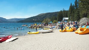 A beach with kayaks and canoes, a lake, and a house in the background. - Kantor's Hideout: Ample TD Home with Private Hot Tub, Pool Table, Walk to Trails (Truckee)