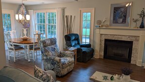 A living room with a fireplace, a dining area with a chandelier, and a large window with curtains. - Shipyard: 271 Evian Island Villa-Relaxing Setting Weekly Rates Discounted (Hilton Head Island)