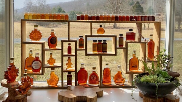 A display of various honey and syrup bottles arranged on shelves by a window with a view of a rural landscape. - Simple.  Rustic.  Luxury. (Monterey)