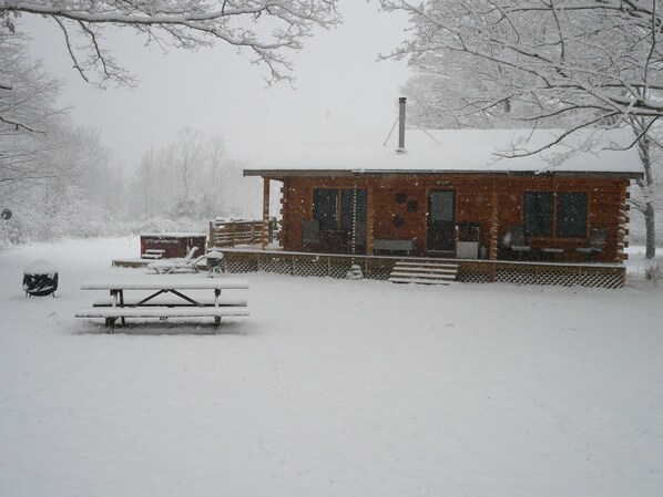 A cabin with a wooden deck, a picnic table, and a snow-covered landscape.