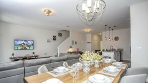 A modern dining area with a wooden table set for six, grey upholstered seating, and a chandelier. - Astonishing Home Private Pool 4830 (Kissimmee)