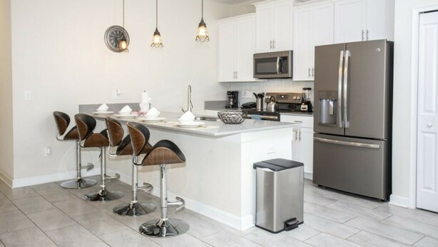 A modern kitchen with white cabinets, stainless steel appliances, and a central island with bar stools. - Astonishing Home Private Pool 4830 (Kissimmee)
