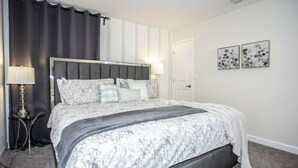 A bedroom with a bed, a nightstand, a lamp, and two wall art pieces. - Astonishing Home Private Pool 4830 (Kissimmee)