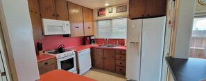 A compact kitchen with wooden cabinets, a microwave, a stove, a sink, and a refrigerator. - OCEANFRONT SINGLE LEVEL HOME- Sleeps 12- Active Discounts -Sorry No Pets Allowed (Oceano)