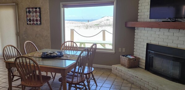A dining area with a glass table, wooden chairs, a fireplace, a television, and a view of the beach. - OCEANFRONT SINGLE LEVEL HOME- Sleeps 12- Active Discounts -Sorry No Pets Allowed (Oceano)