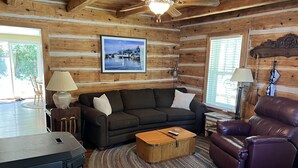 Ein gemütliches Blockhaus-Interieur mit Holzausstattung, Kamin, Sofa, Ledersessel und Teppich.