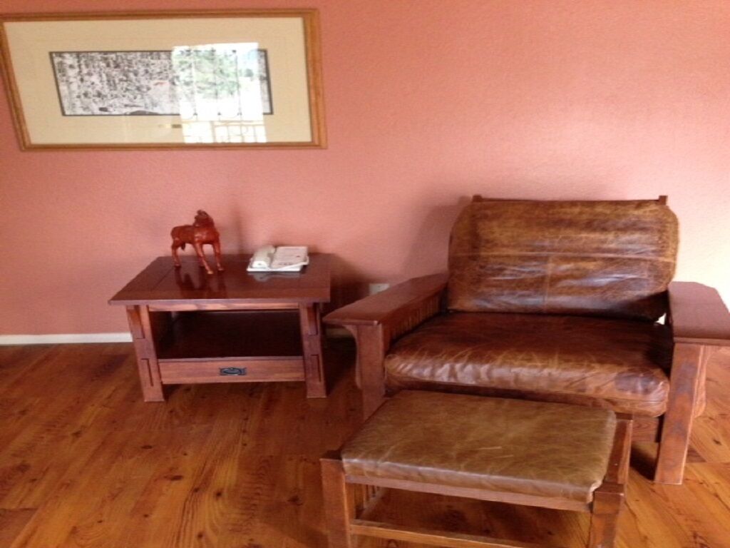 Ein Zimmer mit Holzboden, einem braunen Ledersessel, einem kleinen Holztisch mit Telefon und einer kleinen Pferdefigur sowie einem gerahmten Bild an der Wand.