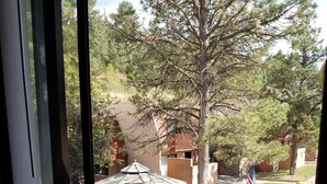 A wooden deck with a round table and two chairs, overlooking a grassy area with trees and a building in the background. - Resort Condo/Relax/ enjoy the outdoors/mountains. Easy access in Winter/ Ruidoso (Ruidoso)