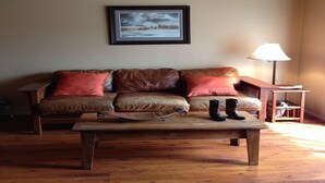 A living room with a brown leather sofa, two red cushions, a wooden coffee table, and a pair of black boots on the table. - Resort Condo/Relax/ enjoy the outdoors/mountains. Easy access in Winter/ Ruidoso (Ruidoso)