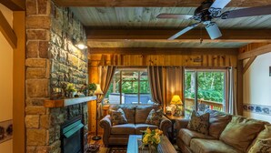 A cozy living room with a stone fireplace, leather sofas, and a wooden ceiling fan.
