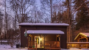 A wooden cabin with a porch, surrounded by snow and trees.