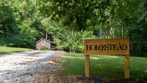 A wooden sign with "HOMESTEAD" written on it, a gravel path, and a house in the background.