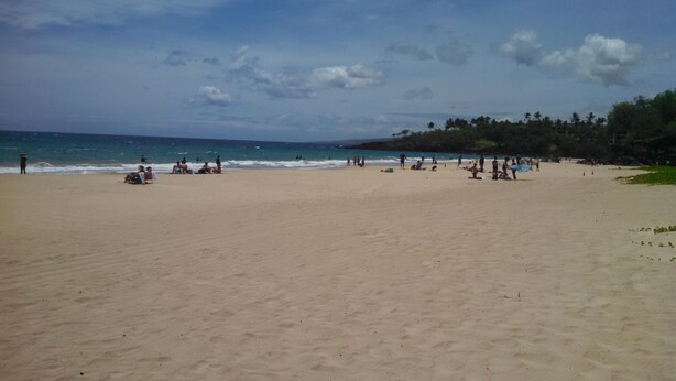 A wide sandy beach with people relaxing and some near the water.