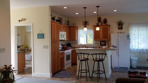 A kitchen with wooden cabinets, a stove, two bar stools, pendant lights, and a refrigerator.