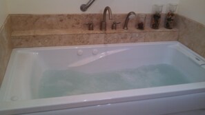 A bathtub with a single faucet and two control knobs, a glass of water, and a glass of dark liquid on the edge. - 1 Bdr 1 Bth  House With Whirlpool Tub (Mountain View)